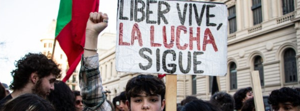 Fotografía. Exterior. Una manifestación en la calle. Una persona levanta el puño y sostiene un cartel que dice "Liber vive, la lucha sigue".